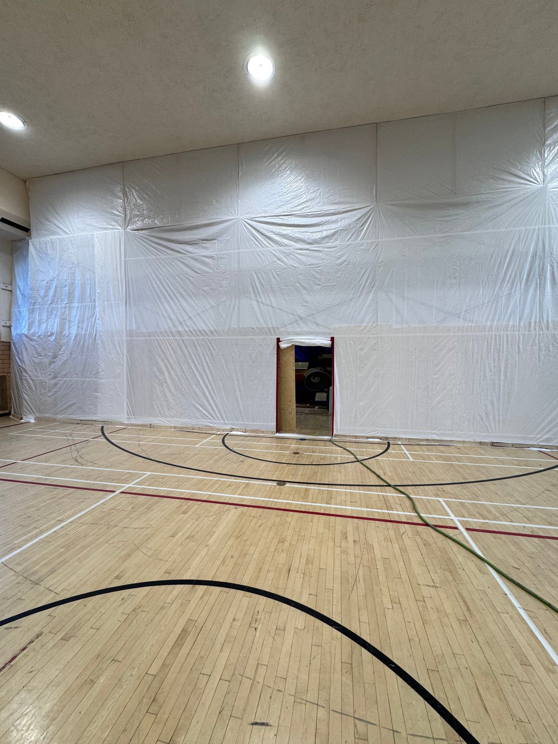 Gymnase dont un mur complet est confiné au polyéthylène, avec une porte d'accès à l'aire de travail