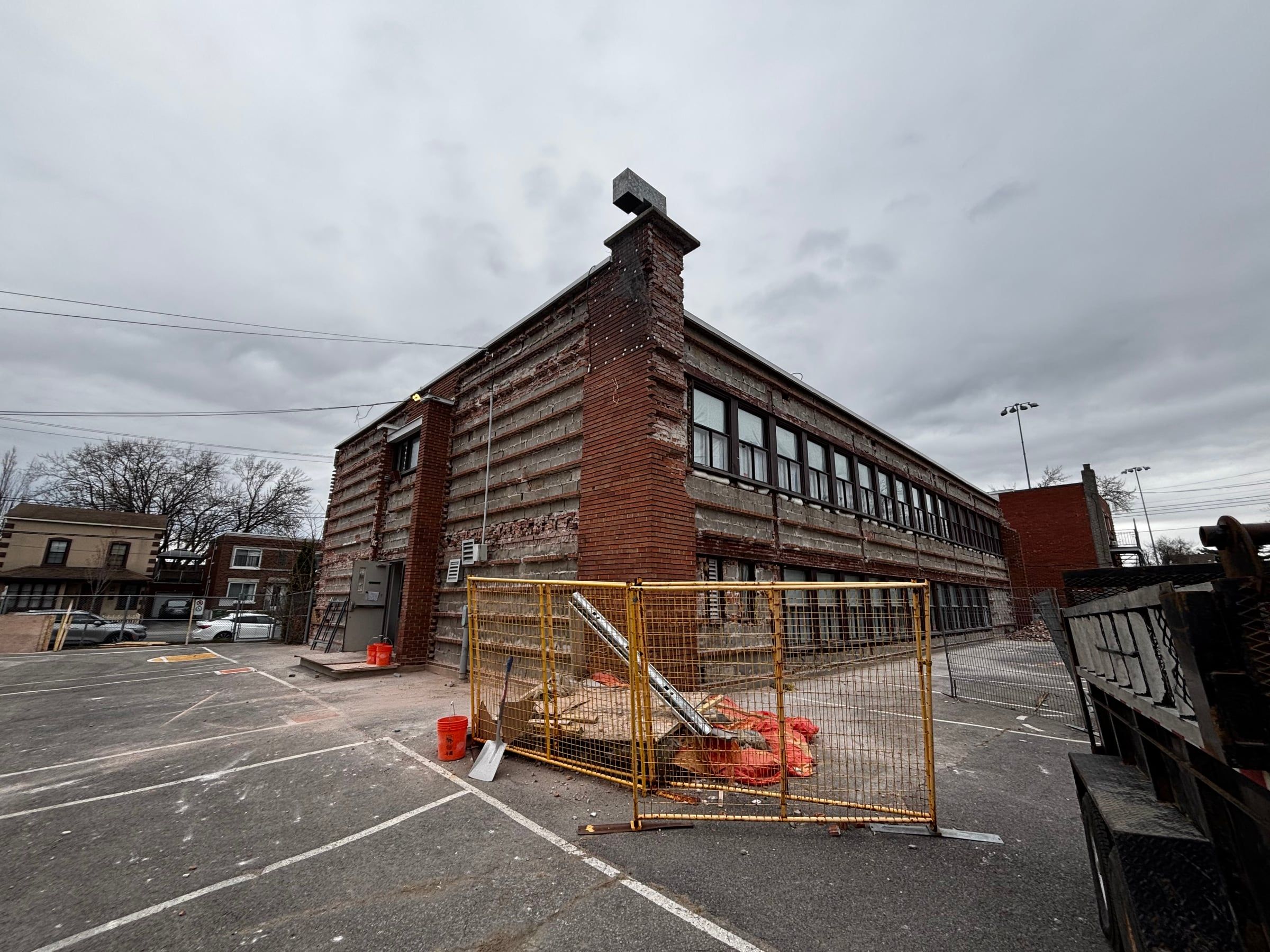 École de deux étages dont le parement de brique extérieur est retiré, aire de travail clôturée au sol